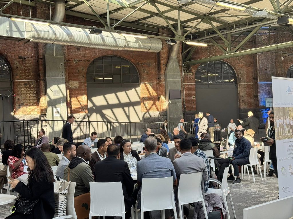 A diverse group of people engaged in discussions at the Global Disability Summit in an industrial-style venue with brick walls and large windows. Participants are seated at round tables, networking and exchanging ideas on inclusion and accessibility.