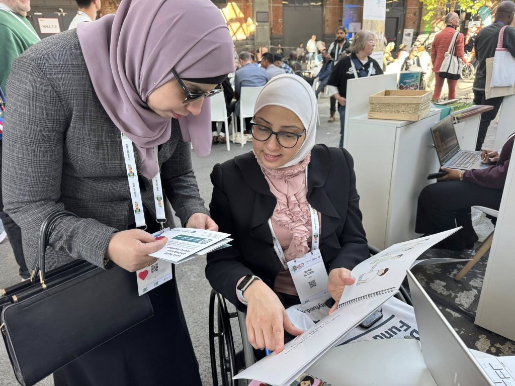 two international delegates (1 on wheel chair and another standing on side) going through the IEC materials made by BYAN